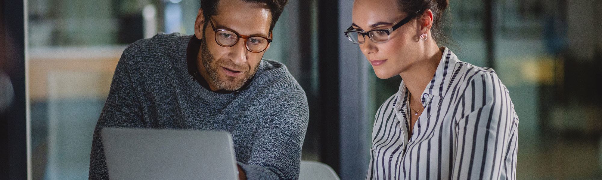 Cropped shot of two business colleagues sitting together and using a laptop in the office late at night