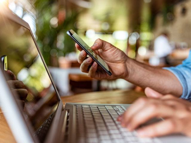 man typing on his phone and his laptop