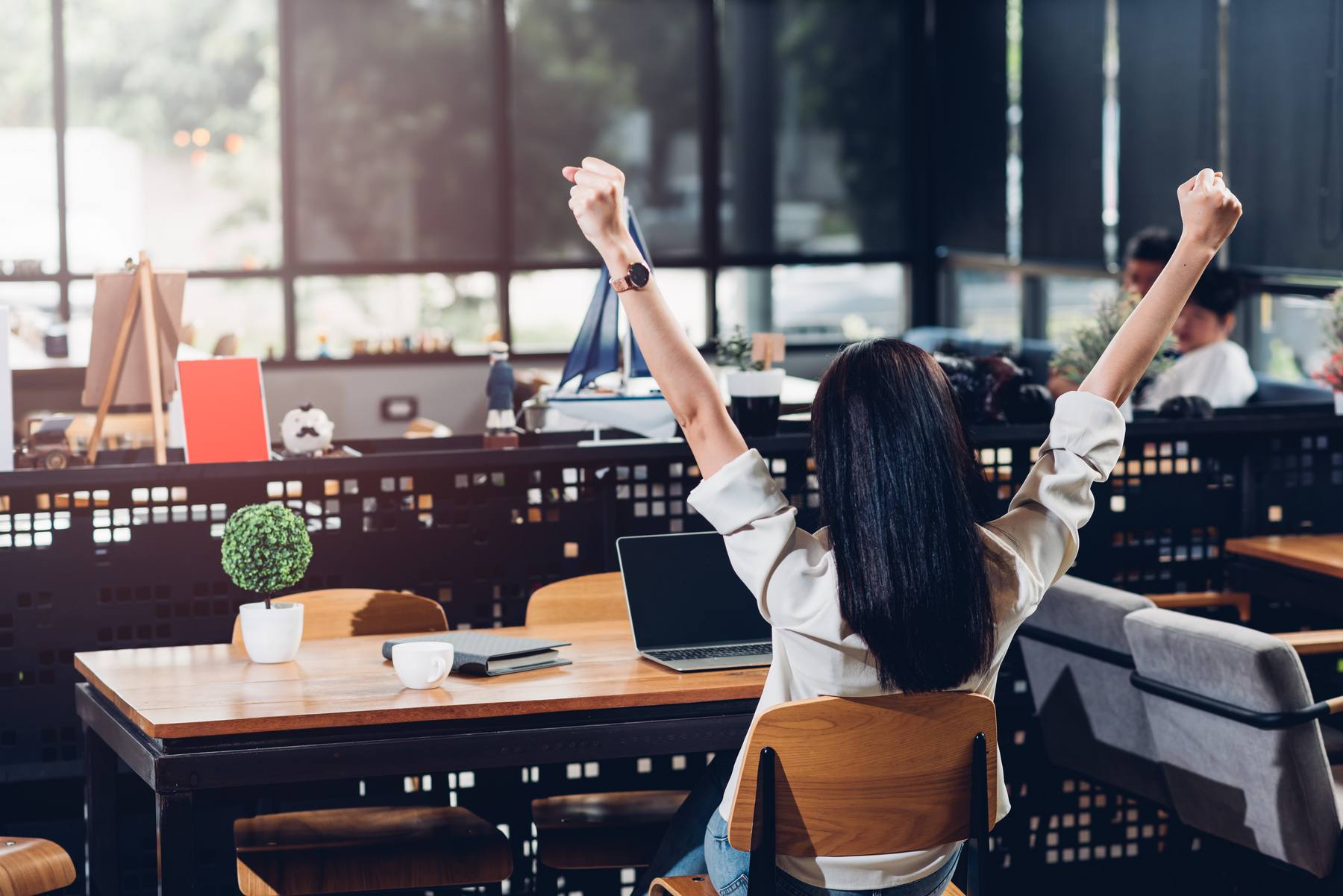 woman in front of laptop with arms raised in happiness