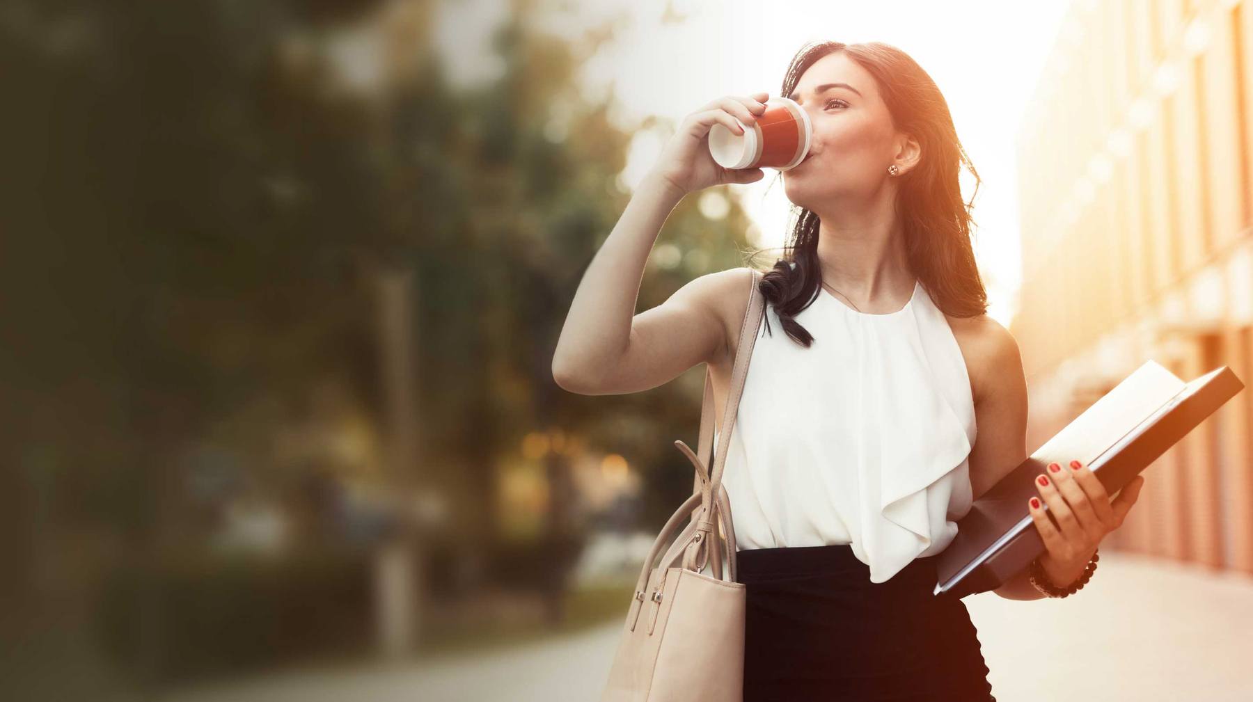 businesswoman walking down the street drinking coffee and holding large book