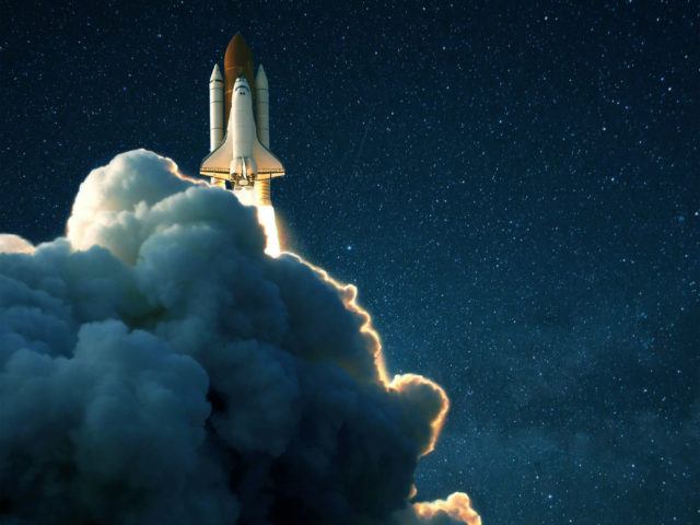 Space rocket launches into space against a starry blue sky. Ship shuttle with clouds of smoke