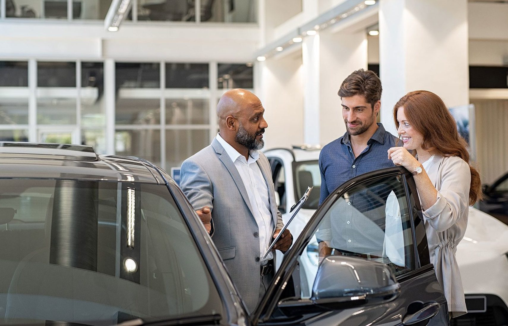 car salesman showing a car to couple in car dealership