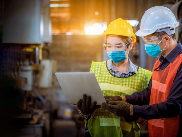 heavy industry workers working on laptop in the middle of factory