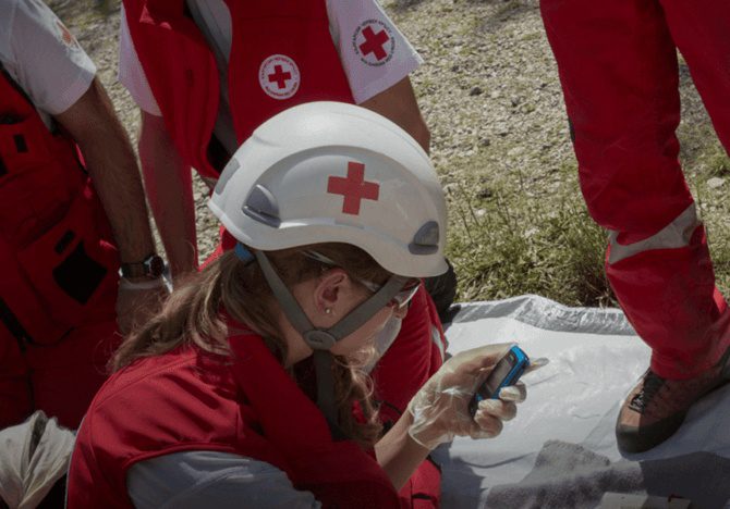 woman in red cross hard hat using her cellular device