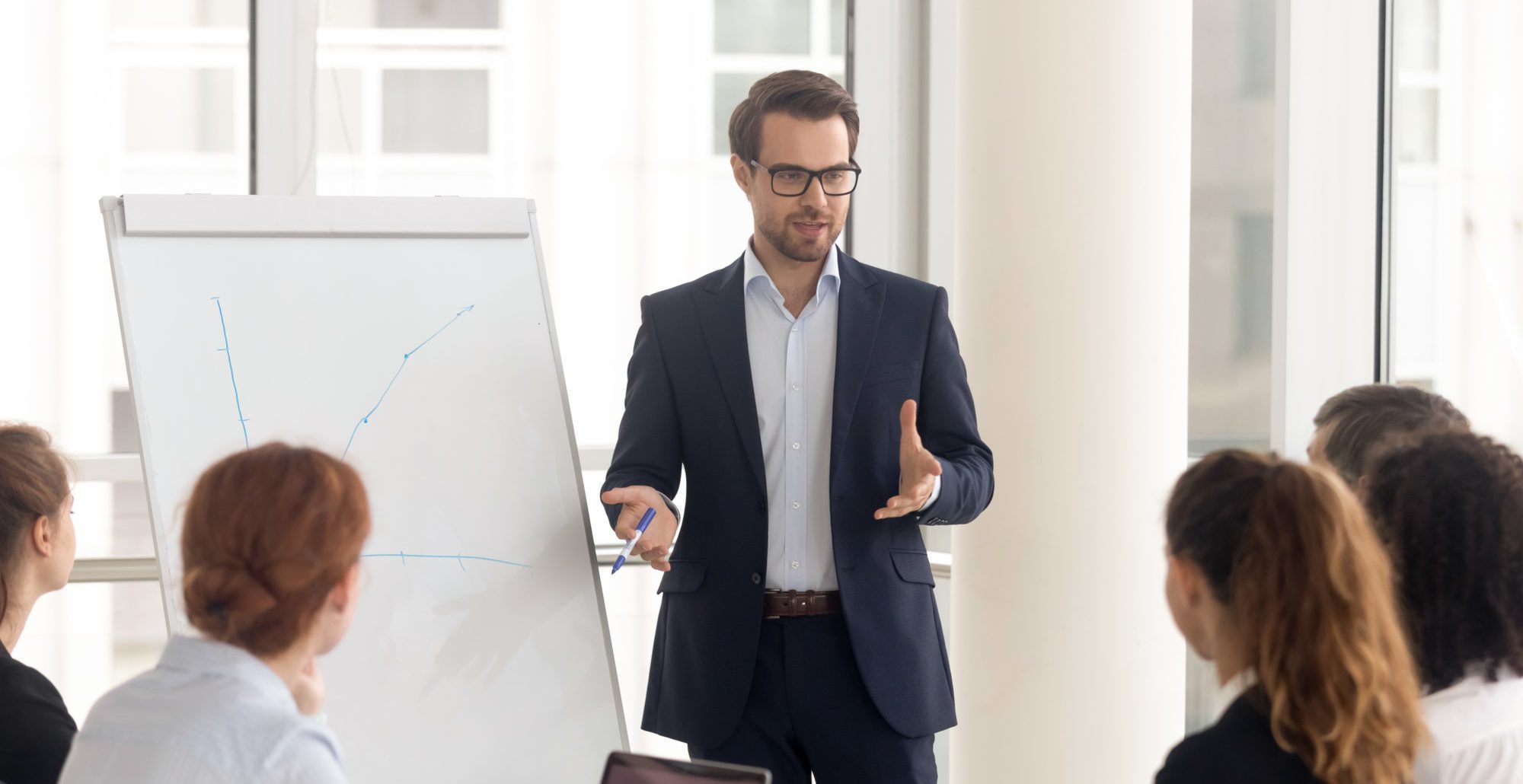 Male business coach speaker in suit give flipchart presentation, speaker presenter consulting training persuading employees client group, mentor leader explain graph strategy at team meeting workshop
