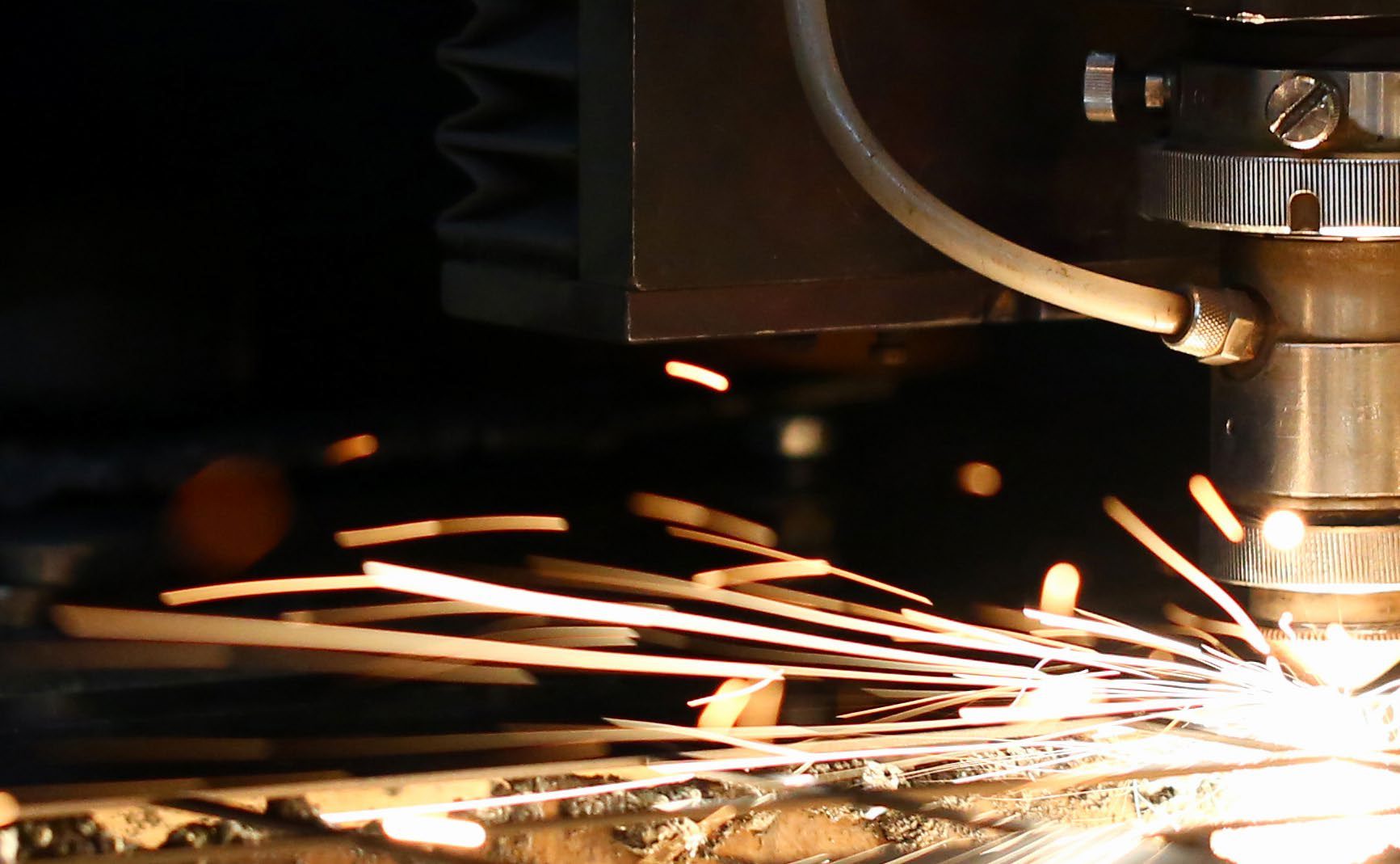 Sparks fly out machine head for metal processing laser metal on metallurgical plant background. Manufacturing finished parts for automotive production concept