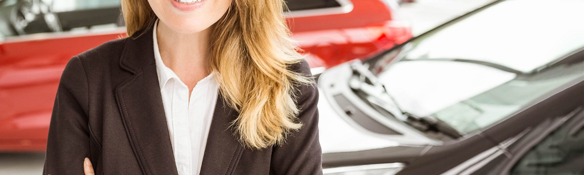 Smiling saleswoman standing with arms crossed in car showroom
