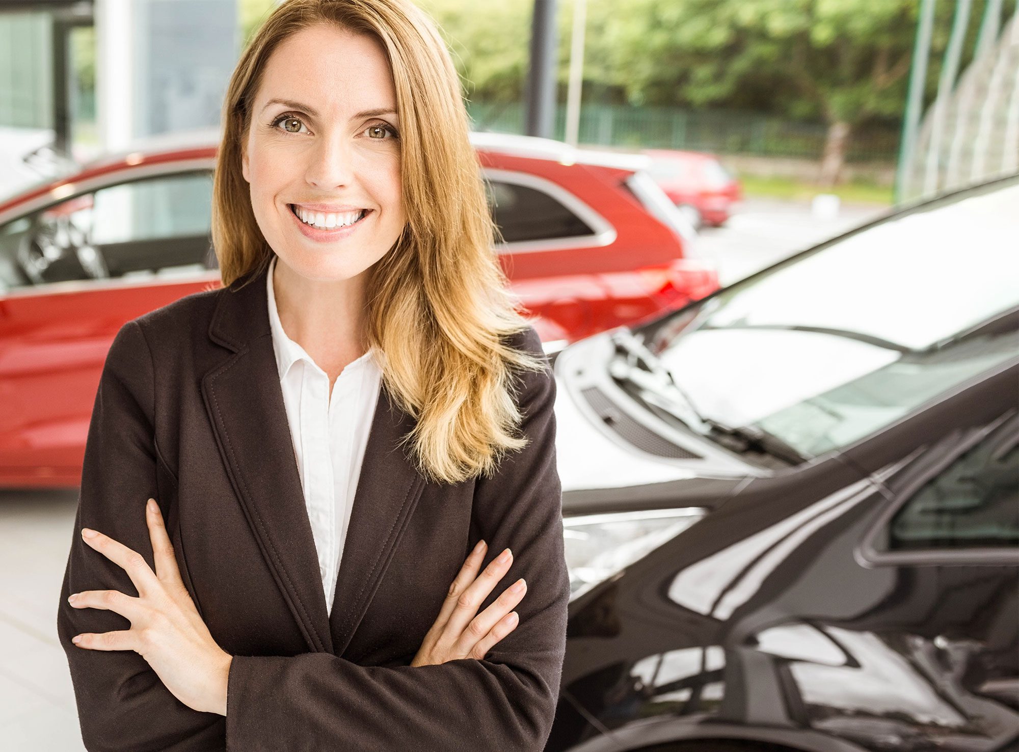 Smiling saleswoman standing with arms crossed in car showroom